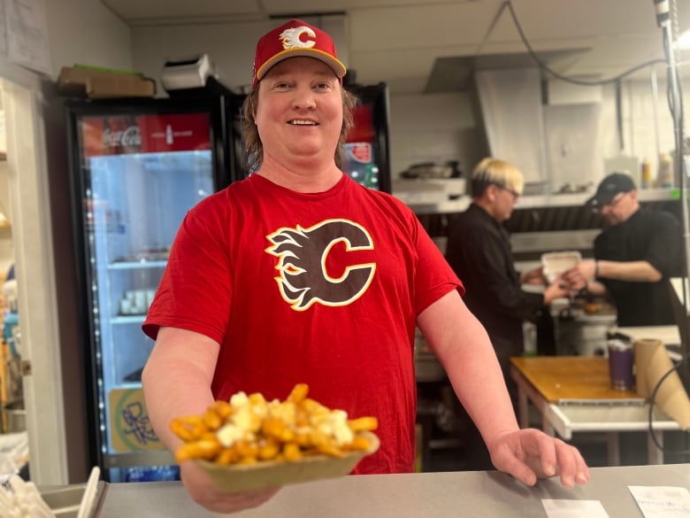 a man wearing a red calgary flames hat and t shirt shows a plate of poutine