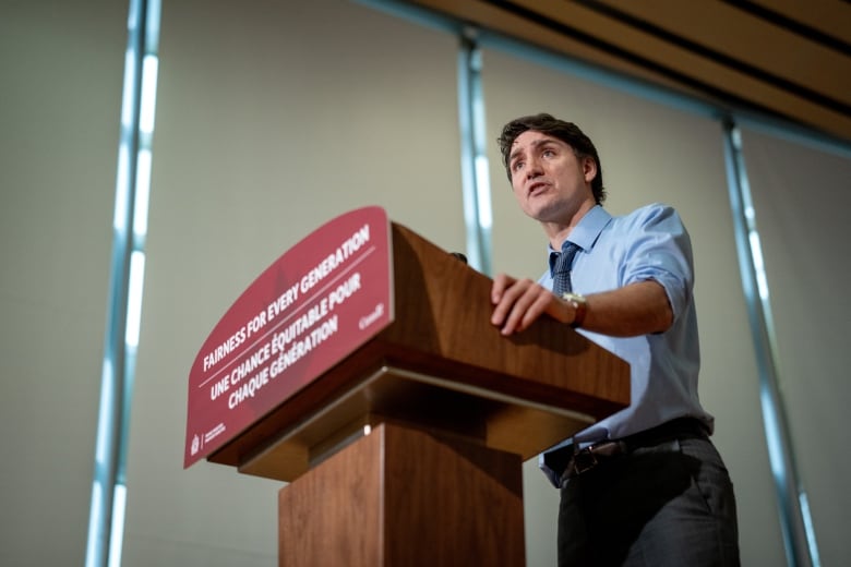 A man in a blue shirt and tie stands and speaks at a podium that reads "fairness for every generation."