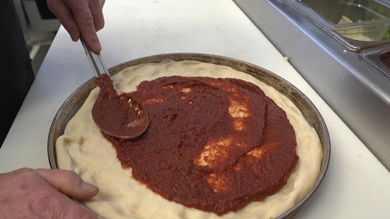 Pizza sauce is spooned and spread onto a crust.