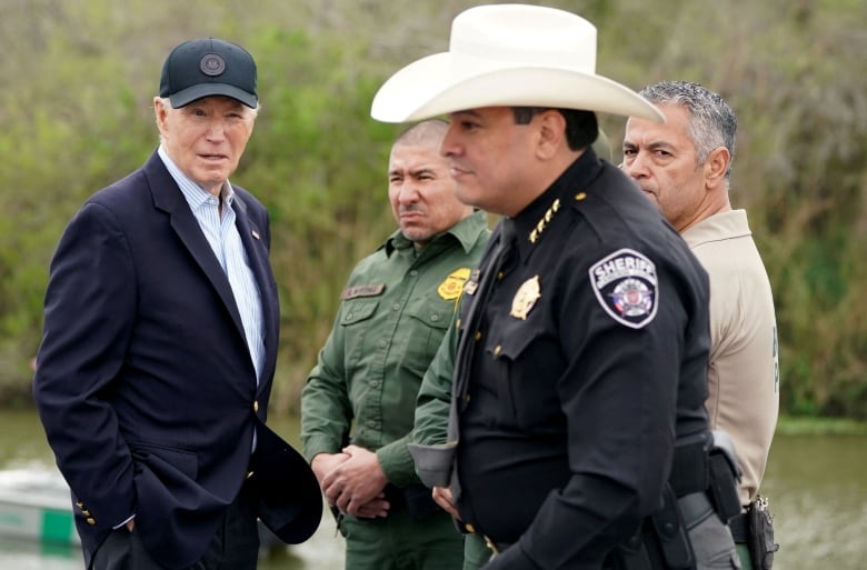 Biden with cap on, surrounded by federal and county authorities. A county sheriff is wearing a white cowboy hat