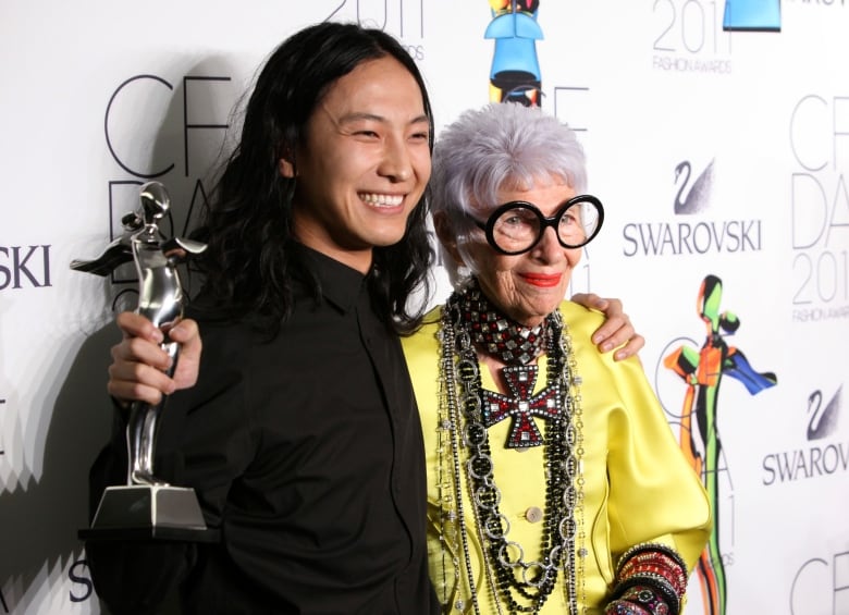 A smiling person holding up an award embraces another person as they pose for a photograph.