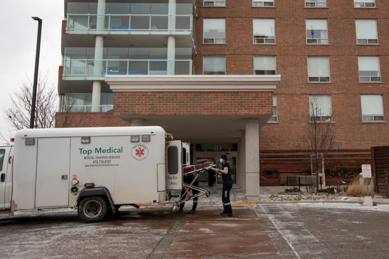 Paramedics load a person on a stretcher into an ambulance outside a long-term care facility on a cloudy day