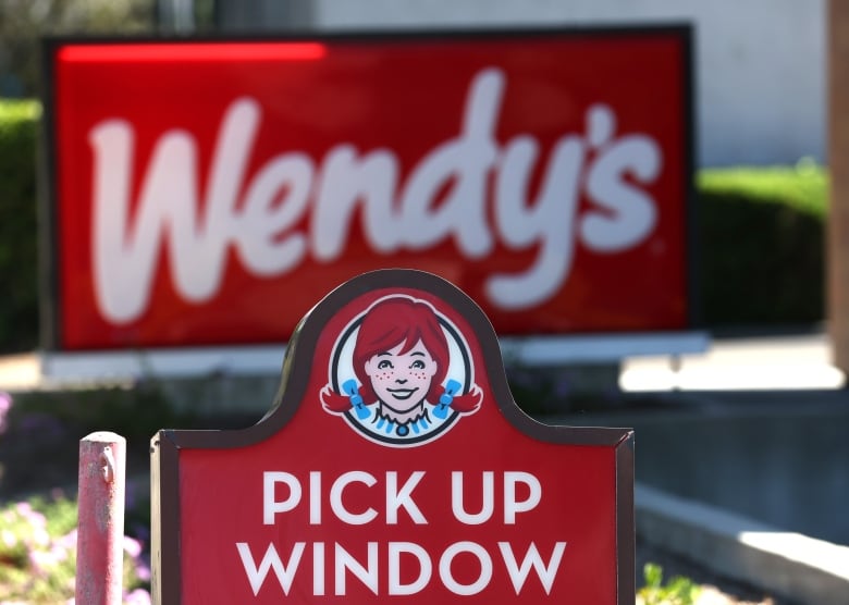 A sign for a Wendy's drive-thru that reads "pick up window" under the chain's logo of a woman with red braided hair.