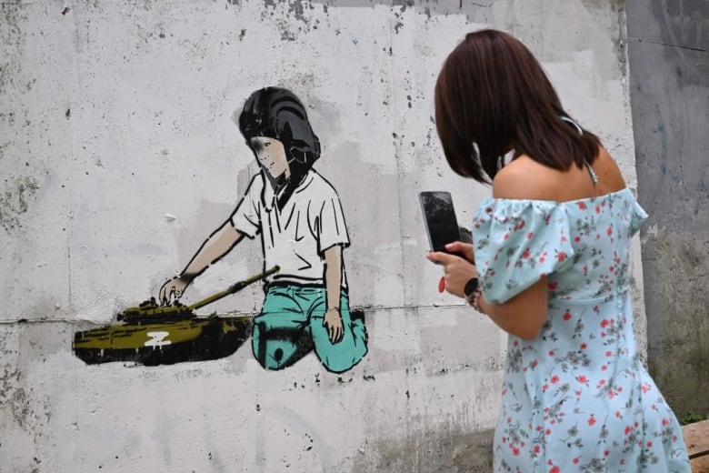 A woman in Vladivostok, Russia, takes a photo of a mural showing a tank marked with a 'Z' on it — the tactical insignia of Russian troops in Ukraine.