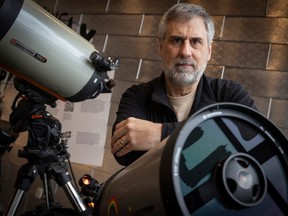 A white man is posing in the background of this photo, in the foreground to his left and in front of him are two microscopes.