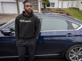 Lamine Sale Nkouendji, a Black man, leans against a blue car wearing a black outfit.