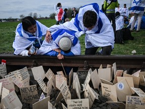 A man draped in the flag of Israel cries by the train tracks, onto which wood signs with written prayers and wishes have been placed, by the former Auschwitz Birkenau Concentration Camp during 35th March of the Living on April 18, 2023 in Oswiecim, Poland.