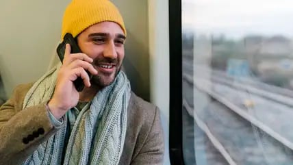 Ein Mann mit einer gelben Mütze sitzt in einem Zug und telefoniert.