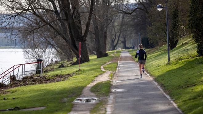 Wetter: Ein Läuferin joggt am frühen Sonntagmorgen bei sonnigem Wetter am Rhein vorbei.