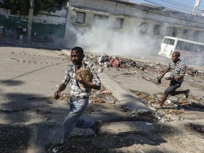 Men run for cover as riot police launch tear gas in an effort to disperse people near the National Palace, in Port-au-Prince, Haiti, Tuesday, April 2, 2024.