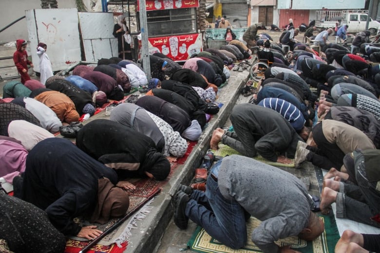 Dozens of people kneel with heads on the floor in a religious ceremony in an urban setting. 