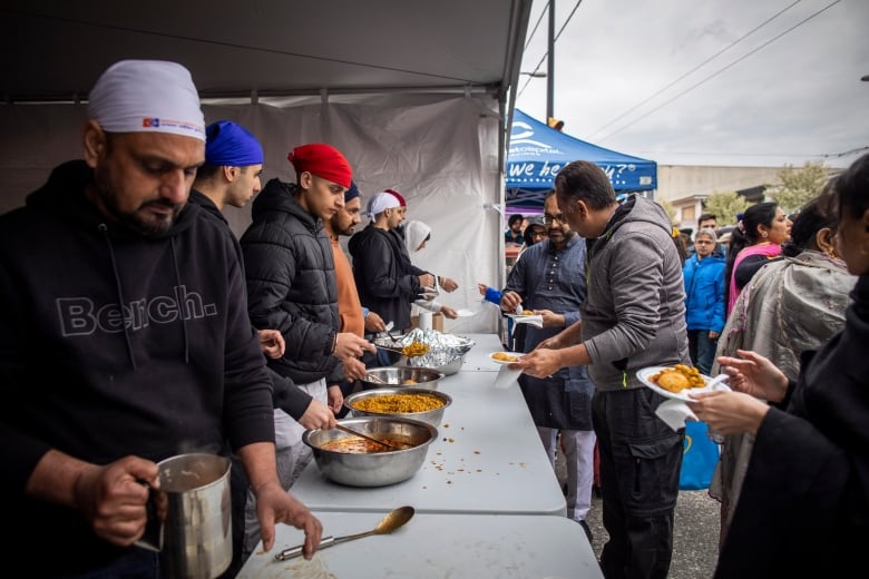 People are seen at the front of a queue to get food from a tent at a Sikh parade.