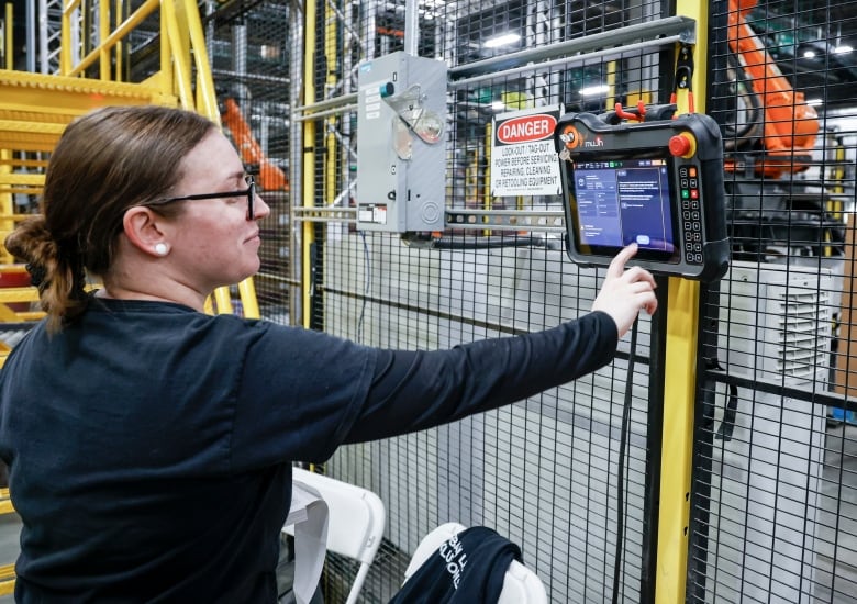 a woman in a blue shirt pushes a button on an electric panel in a warehouse