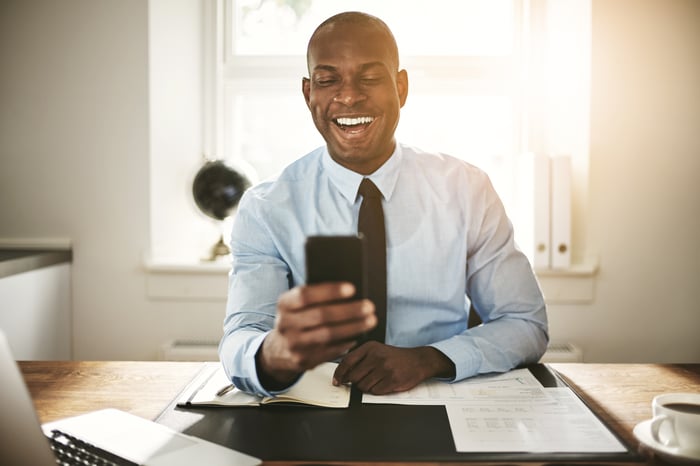 An investor smiles while looking at a phone in an office.