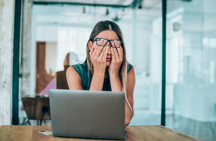 A person with hands over face while sitting in front of a computer.