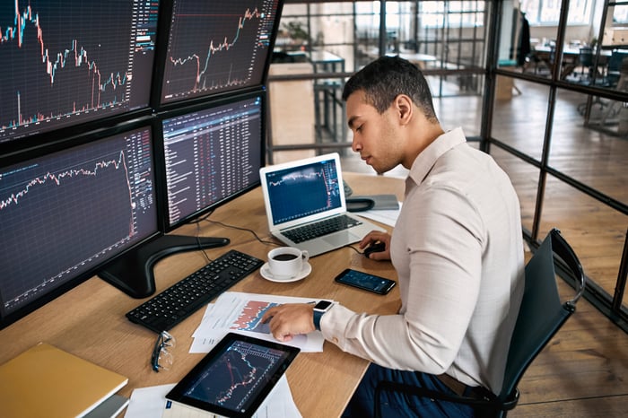 An investor looks at several screens on their desk.