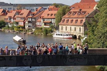 Touristen stehen auf der Rathaus-Brücke an der Regnitz und betrachten das Rathaus von Bamberg.