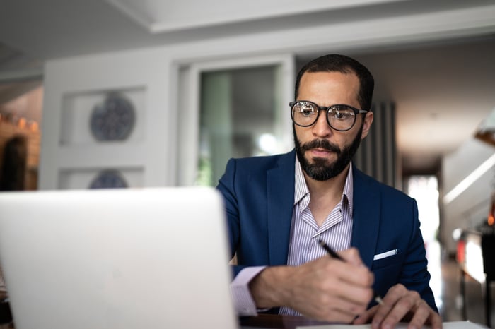 Person looking at laptop and writing note.