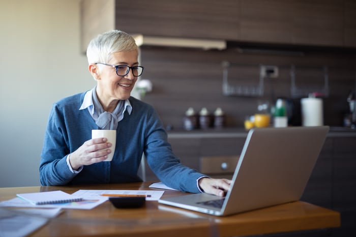 A person looks at a laptop while holding a coffee mug.