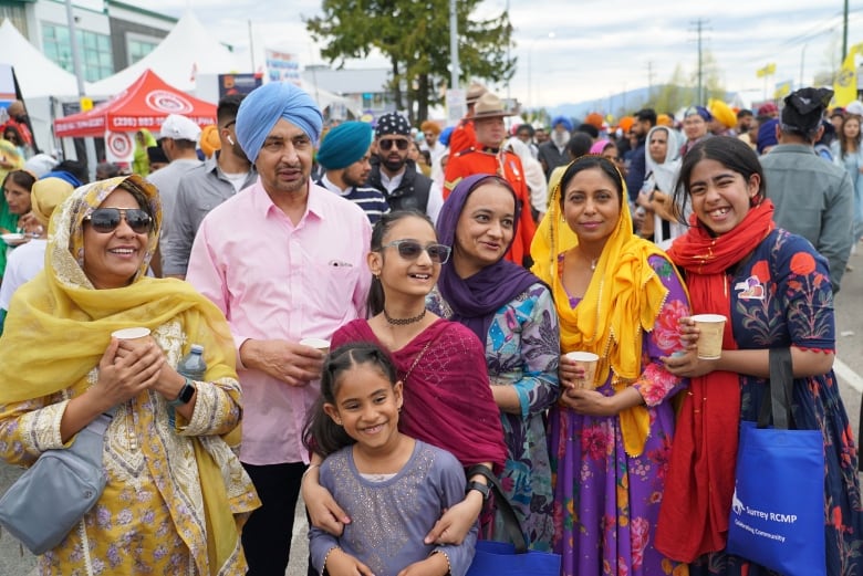 A family adorned in bright colours smile and laugh in a crowd.