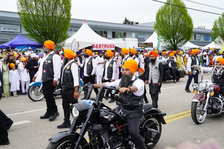 Men on motorcyles walk and ride in a crowd.