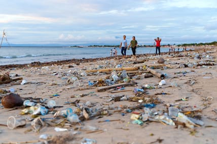 Urlaubende spazieren zwischen Müllbergen an einem Strand auf Bali.