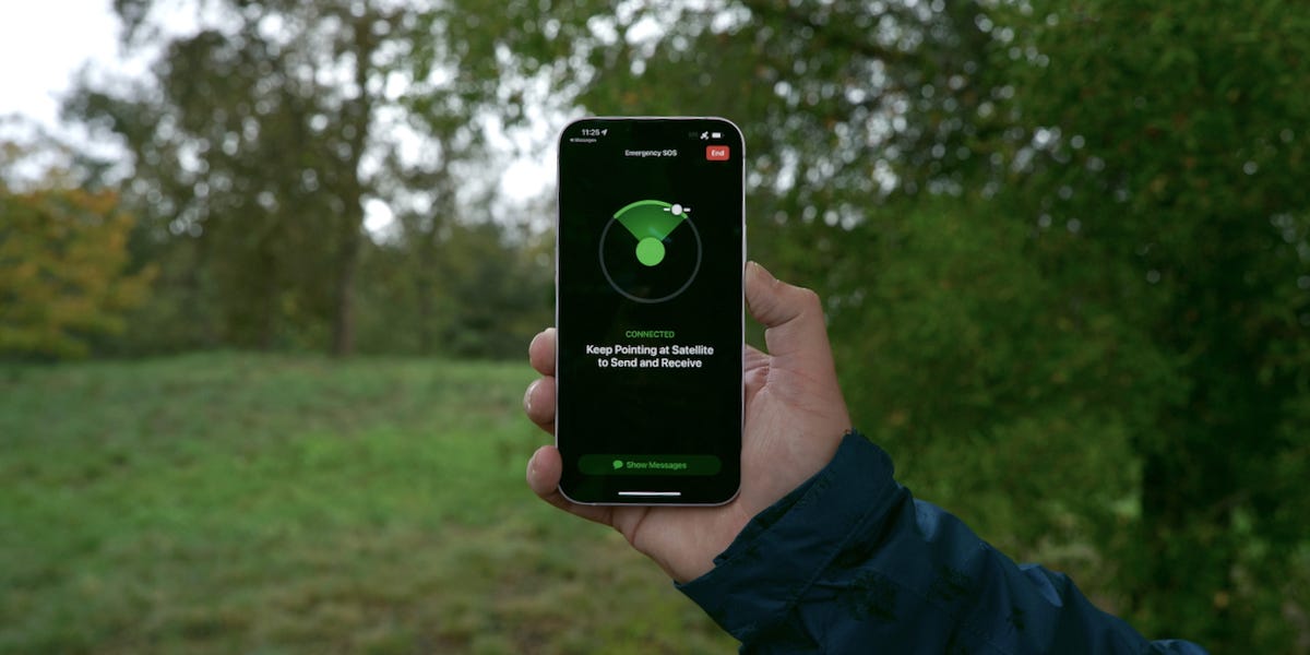 person holding up an iPhone with a radar-like satellite finding feature, with trees in background