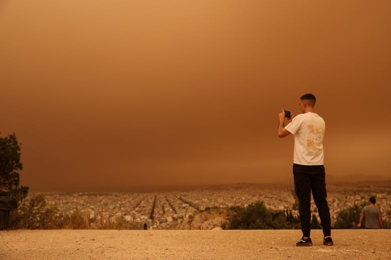 A man takes a photo of orange skies