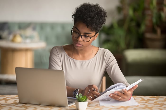 Person looking at a laptop and writing in a notebook.