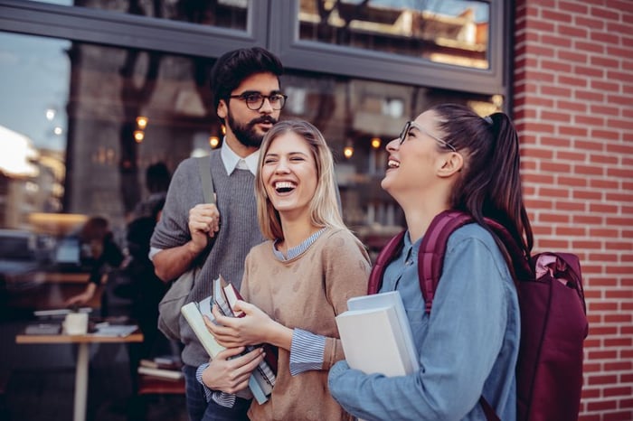 Three Students Walking Together Carrying Their Books And Laughing