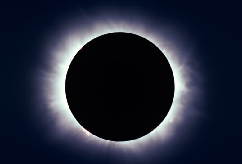 A black circle is surrounded by a halo of light against a dark background. 