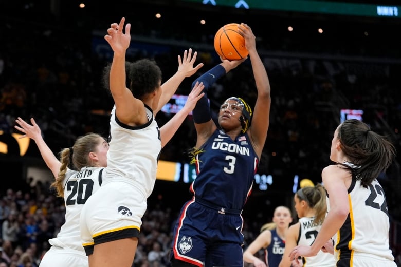 A basketball player shoots a jump shot as two opponents try to block her.