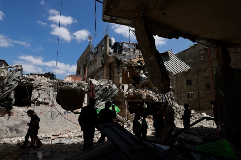 People walk past or gather around a heavily damaged building.