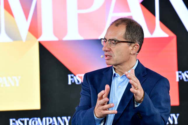 Stephane Bancel speaking with his hands up, Fast Company logos on the backdrop behind him