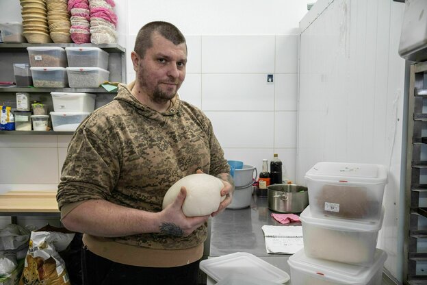 Ein Mann hat einen Kugel Teig in der Hand, er steht in der Küche