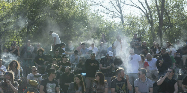 eine große Gruppe Menschen sitzt im Görlitzer Park in Berlin und kifft, dicke Rauschschwaden steigen auf