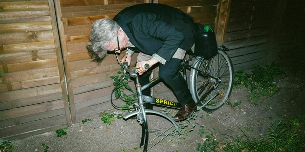 Ein Mann mittleren Alters sitzt auf einem Fahrrad, das nicht fährt, weil ihm das Vorderrad fehlt