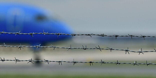 Hinter Stacheldraht Rollt ein Flugzeug auf die Startbahn.