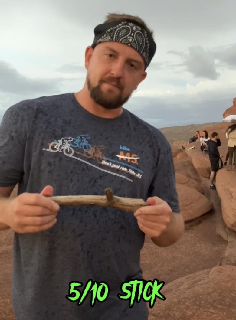 A man with a bandanna around his head stands in a rocky area holding a small, stubby stick and frowning. Green text reads: "5/10 stick."