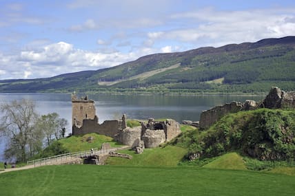 Blick auf die Ruinen von Urquhart Castle am schottischen Loch Ness, im Hintergrund grüne Hügel