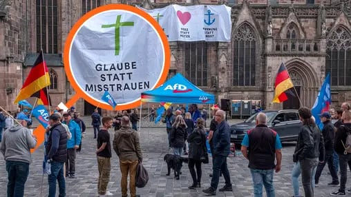 Eine Wahlkampfkundgebung vor einer Kirche, an der ein Transparent hängt mit dem Schriftzug: "Glaube statt Misstrauen, Herz statt Hetze, Hoffnung statt Angst"