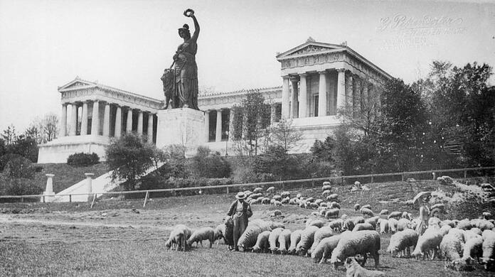 1905 auf der Theresienwiese unterhalb der Bavaria: Hier macht die Wiese mitten in der Stadt ihrem Namen noch alle Ehre, weshalb auch der Schäfer hier seine Herde noch ausgiebig weiden lassen kann. Angesichts der geteerten Straßen und ganzjähriger Dauernutzung durch Veranstaltungen ist die Wiesn ja heute längst &ndash; um Sigi Sommer zu bemühen &ndash; zur "Asphaltn" verkommen.