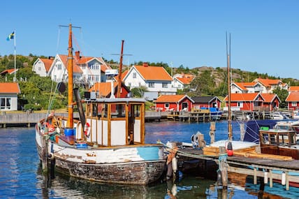 Idyllisches schwedisches Westküstemdorf mit weißen Häusern und roten Dächern vor einem Hafen, in dem Boote liegen