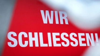 Der Schriftzug «Wir schließen!» steht hinter einem Rollgitter an einem geschlossenen Geschäft. 