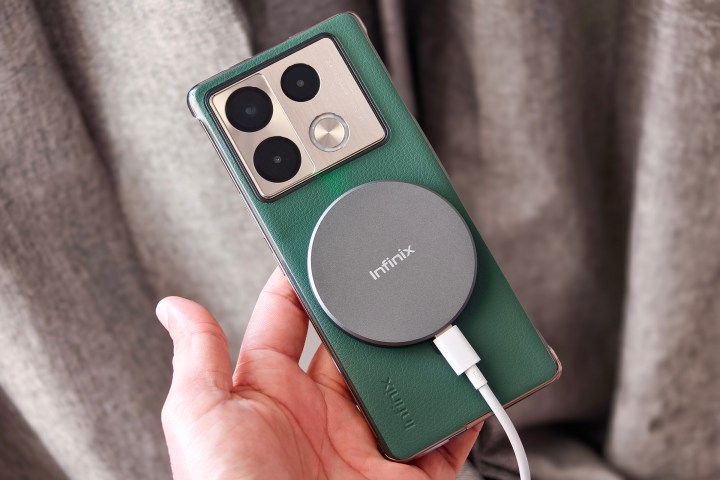 Wireless charging puck attached to a green Infinix Note 40 Pro+ on a jute stool.