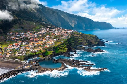 Luftblick auf den Küstenort Seixal auf Madeira, der sich über die grünen Klippen zieht, darunter der tosende Atlantik