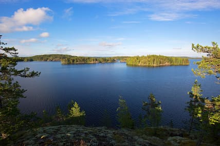 Einer der Saimaa-Seen an der finnischen Seenplatte im abendlichen Sommerlicht mit grünen Wäldern im Hintergrund