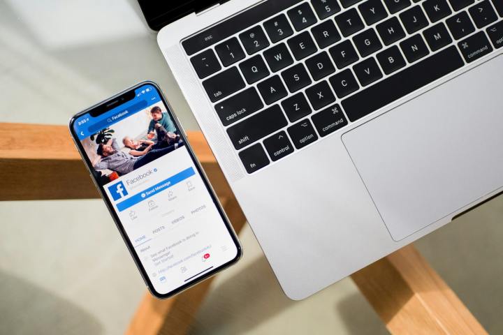 An iPhone next to a MacBook. The iPhone is displaying the Facebook app.