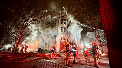 A burning apartment building with firefighters standing outside