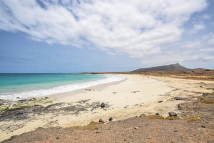 Blick auf einen hellen Sandstrand und das türkisfarbene Meer auf Maio, Kapverden, dahinter karge Hügel